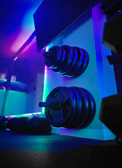Barbell with weights on a rack in a gym with colorful LED lights. Gym interior with colourful LED lights and equipment. Personal Training in West London Southall UB1 at VIP studio 4 mins away from Southall Station with Free Parking